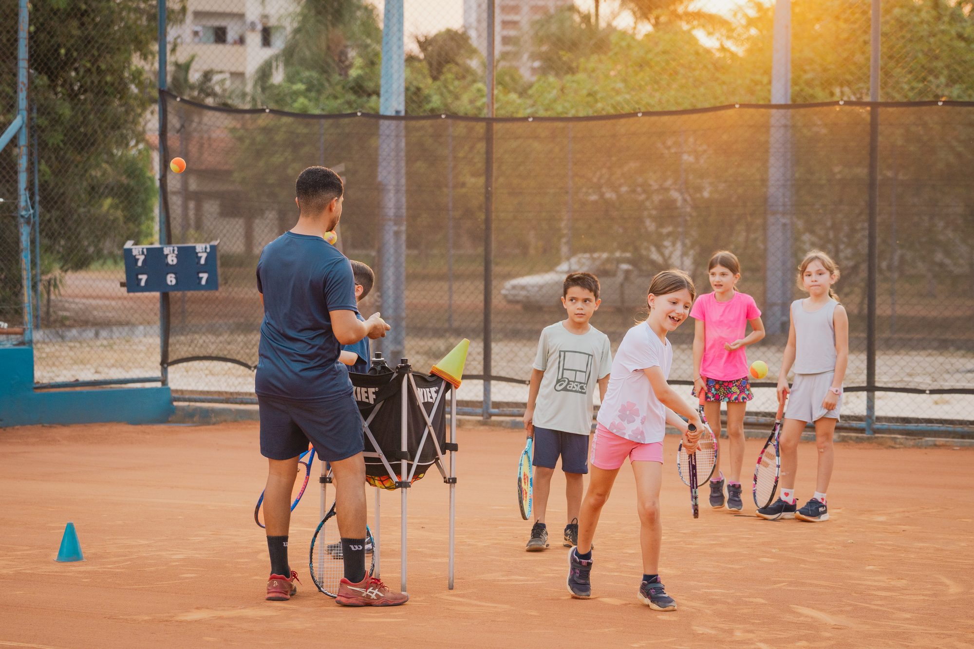 Turma de crianças em treino noturno na quadra de saibro